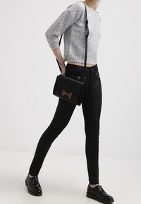 Osoba oblečená v šedém zkráceném svetru, černých skinny kalhotách, černých botách a nesoucí černou crossbody tašku s kovovým zapínáním.