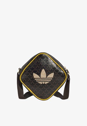 Sort firkantet skuldertaske med gul kant, med et stort beige Adidas trefoil-logo og små gentagne logoer i baggrunden.