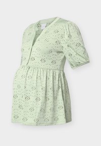 Ανοιχτό πράσινο μπλουζάκι εγκυμοσύνης με κοντά φουσκωτά μανίκια, διακοσμητικό μοτίβο με οπές και λουλούδια, κουμπωτό μπροστινό μέρος και λεπτομέρεια ζώνης στη μέση.