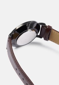 Brown leather strap watch with a black stainless steel case, round shape, polished finish, and a visible crown on the right side.