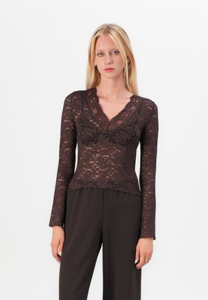 Haut à manches longues en dentelle marron avec un décolleté en V profond et un motif floral, superposé sur une base sombre unie. Présente une silhouette ajustée et une texture délicate.