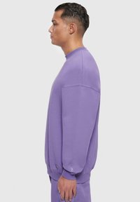 Lila Sweatshirt mit Rundhalsausschnitt, langen Ärmeln und gerippten Bündchen. Verfügt über eine dezente Markenkennzeichnung am Bündchen und hat eine lässige Passform.