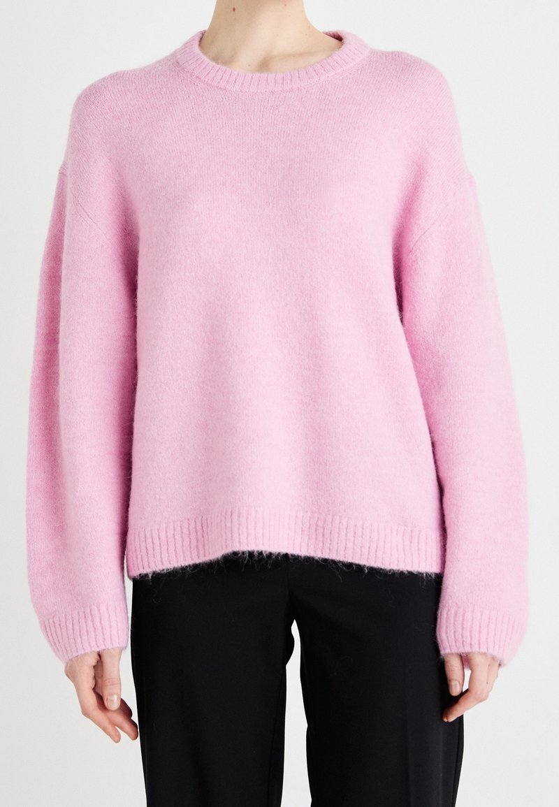 Pink knitted sweater with a round neck, relaxed fit, and ribbed cuffs and hem. Soft, fuzzy texture adds depth to the design.