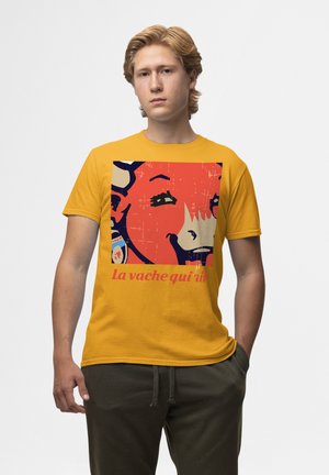 Gul bomulds t-shirt med en grafisk print af en smilende ko med blå accenter og teksten "La vache qui rit" i pink.
