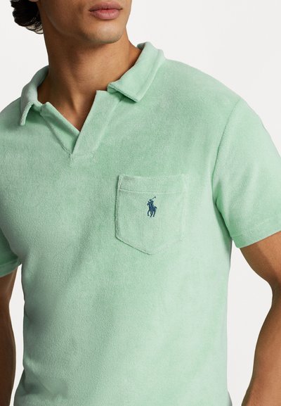 Polo shirt in mintgroene handdoek stof met een kraag en een zak met een marineblauw geborduurd logo op de bovenste linkerzijde.
