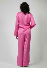 Set di pigiama in satin rosa con maniche lunghe e pantaloni a gamba larga, caratterizzato da una superficie liscia e dettagli a contrasto sull'orlo.