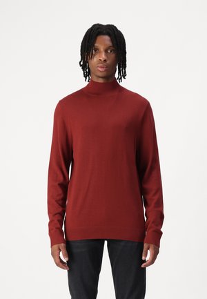 Bordeauxfarbener Rollkragenpullover mit langen Ärmeln und gerippten Bündchen. Weiche, glatte Textur, taillierter Schnitt und gerade Saum. Getragen mit dunklen Jeans.