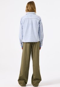Lichtblauwe denim jas met patroon, lange mouwen, aansluitende schoudernaad en zijschuven. Gecombineerd met losse olijfgroen broeken.