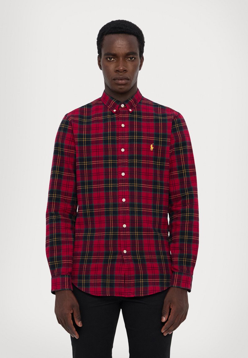 Κόκκινο καρό πουκάμισο με κουμπιά, φτιαγμένο από βαμβάκι, με κίτρινες και μαύρες λεπτομέρειες, διαθέτει κλασικό γιακά και μακριά μανίκια, συνδυασμένο με σκούρα παντελόνια.