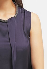 Purple satin top featuring a textured beaded collar, a draped design at the neckline, and sleeveless construction for a lightweight appearance.