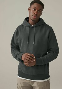 Sudadera gris oscuro con un bolsillo canguro frontal, capucha con cordón, puños y dobladillo acanalados. Fabricada con una suave tela texturizada.