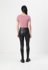 Rosa kortärmad topp kombinerad med svarta leggings i konstläder. Outfiten kompletteras med svarta klumpiga skor. En vit bakgrund framhäver detaljerna.