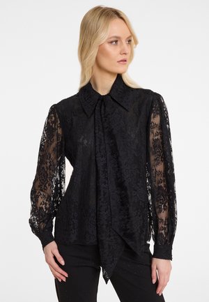 Zwarte kant blouse met lange, doorzichtige mouwen, een spitse kraag en een gestrikt detail aan de voorkant, met florale patronen en een vloeiende silhouette.