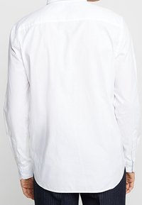 Witte, lange mouwen shirt met een kraag, manchetten met knopen en een gladde textuur. Heeft een licht gebogen zoom en subtiele stiksel details.