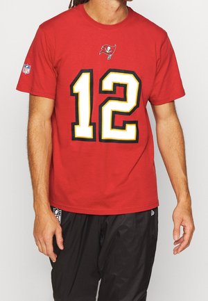 Camiseta roja de manga corta con un gran número negro y amarillo "12" en el frente, con un logo de los Buccaneers encima y una insignia de la NFL en la manga.