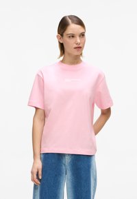 Roosa puuvillane T-särk lühikeste varrukatega ja ümmarguse kaelusega. Rinnal valgete trükitud logo tekstiga. Vaba lõike ja siledapinnaline.