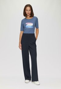 T-shirt bleu à manches courtes avec une impression graphique et du texte, associé à un pantalon large taille haute noir marine et des baskets blanches.