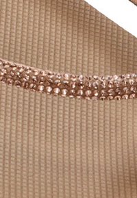 Tejido beige con una textura acanalada, que presenta una fila de pequeñas cuentas brillantes de oro rosa a lo largo del borde superior.