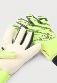 Guantes de portero verdes y negros con agarre texturizado, palma de látex blanca, dedos acolchados y una correa ajustable en la muñeca con la etiqueta "ULTRA".