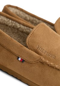 Mocassini in suede marrone, slip-on, con fodera in shearling, logo ricamato e un piccolo dettaglio tri-color vicino al tallone.