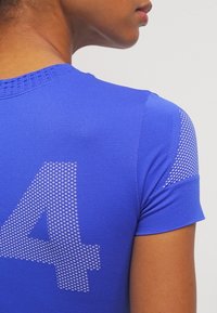 Camiseta atlética azul de manga corta, con un cuello redondo texturizado y un gran número "4" en un patrón de puntos en la parte posterior.