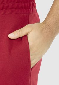 Rode joggingsbroek van een katoenmix met een zijzak en een elastische tailleband, met een gladde textuur en minimale stikdetails.