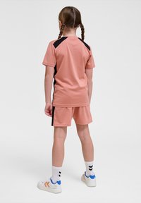 Ensemble de vêtements de sport pêche avec manches courtes et shorts assortis, ornés d'accents noirs sur les côtés. Les compléments incluent des chaussures blanches avec des détails colorés.