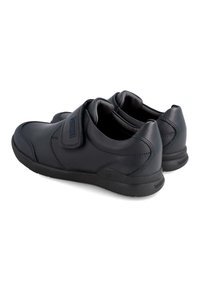 Zapatos de cuero negro con una superficie lisa, puntera redondeada, correa de velcro y cuello acolchado; suela de goma con detalle de tread texturizado.