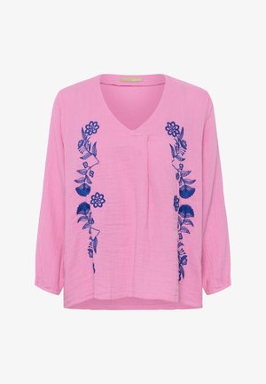 Blouse rose à manches longues avec col en V et broderie florale bleue le long des côtés avant.
