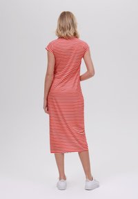 Robe midi rayée rouge et blanche avec des manches courtes, forme ajustée, texture lisse et fente à l'ourlet. Associée à des baskets blanches.