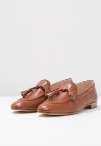 Bruine leren loafers met franjes, ronde neus en subtiele stiksels. Platte houten hak, gladde afwerking en instapmodel.