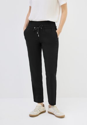 Zwarte elastische broek met een trekkoord, twee voorzakken, tapered leg ontwerp, gecombineerd met lichtgekleurde sneakers.
