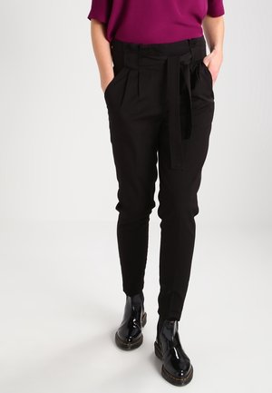 Zwarte tapered broek met een riem, voorzien van een gladde textuur en een geplooid front, gecombineerd met glanzende zwarte enkellaarsjes.