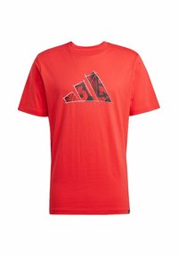 T-shirt in cotone rosso con un design grafico che presenta accenti neri e grigi in un motivo triangolare sul petto. Maniche corte, collo a giro.