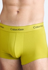 Zeleni bombažni bokser kratke hlače z prilegajočim dizajnom in črnim logotipom "Calvin Klein" na elastičnem pasu. Gladka tekstura, dolžina do sredine stegna.