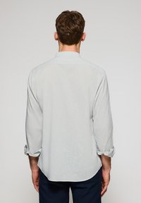 Ljusblå långärmad skjorta, mjukt tyg, knappad krage, rullade ärmar, rundad fåll och subtil struktur synlig på baksidan.