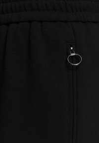 Zwarte joggingsbroek van een textiel met structuur, met een elastische tailleband en een met rits afgesloten zak met een ronde trekknop.