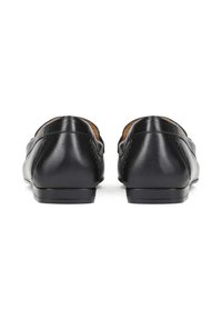 Par de mocasines negros de cuero sin cordones vistos desde atrás sobre un fondo blanco.