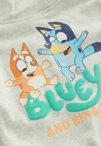 Szara bluza z kapturem z postaciami z kreskówek Bluey i Bingo. Napis w odcieniach niebieskiego i pomarańczowego brzmi "BLUEY I BINGO."