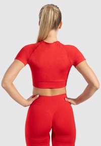 Rode cropped top met korte mouwen en een geribbelde zoom, gecombineerd met hoge taille rode leggings met een naadloos ontwerp en een accentueerde achterkant.