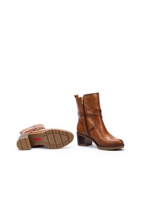 Bottines en cuir marron avec une fermeture éclair sur le côté, un talon empilé et une semelle en caoutchouc texturée. Présente un détail de sangle entrecroisée.