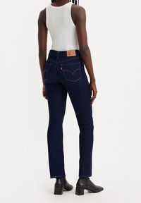 Jeans de denim azul oscuro con corte slim, que cuentan con bolsillos traseros, costuras en contraste y una etiqueta de cuero de la marca en la cinturilla.