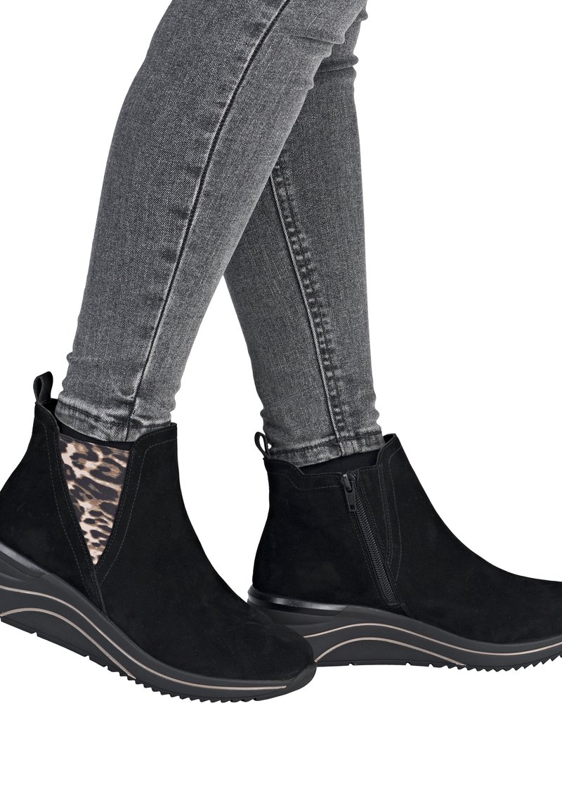 Bottines en suède noir avec un talon compensé, dotées d'un panneau latéral élastique à imprimé léopard et d'une fermeture éclair. Portées avec un jean skinny gris.
