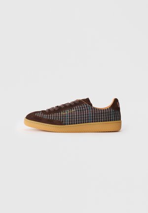 Zapatilla baja con ribete de ante marrón, parte superior de tela de cuadros houndstooth, suela de goma, punta redondeada y logo dorado "Paul Smith" en el costado.