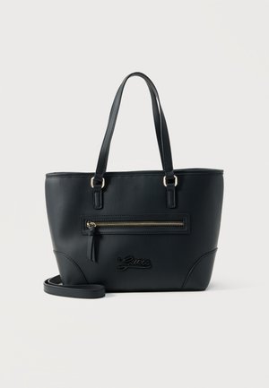 Sac cabas noir Guess avec double poignée, poche avant zippée et bandoulière amovible sur fond blanc.