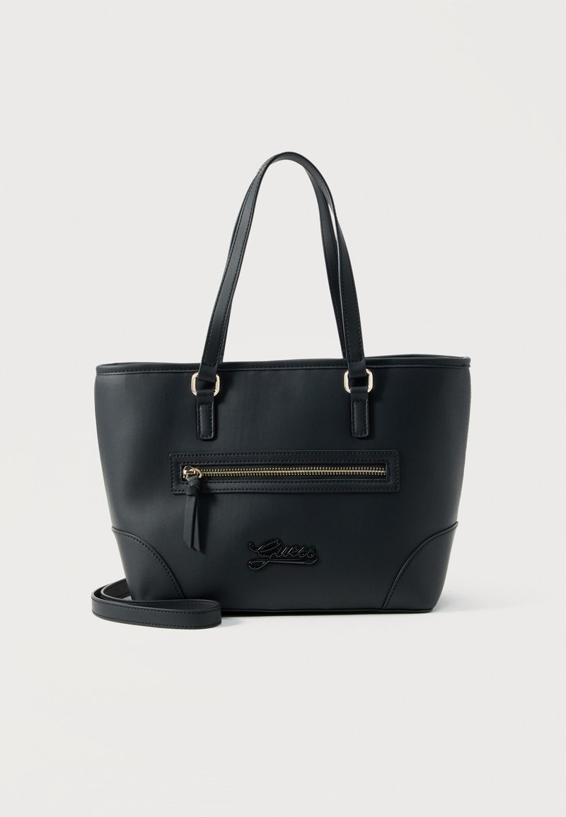 Μαύρη τσάντα Guess tote με διπλές λαβές, μπροστινή τσέπη με φερμουάρ και αποσπώμενο λουρί ώμου σε λευκό φόντο.