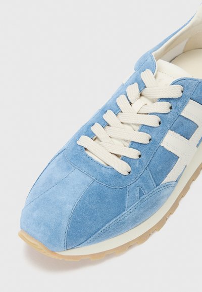 Sinine seemissneaker valgete paelte, valgete külgribade ja beeži kummitaldadega valgel taustal.