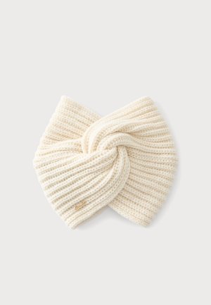 Cream-colored knitted headband with twisted knot design and small gold logo tag on a plain light background.
