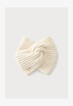 Bandeau tricoté couleur crème avec un nœud torsadé et une petite étiquette logo dorée sur un fond clair uni.