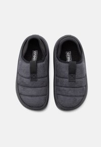 Un set de papuci de interior negri, cu aderenta, cu un tabul de prindere si o parte superioara din material texturat si moale, prezentati dintr-o perspectiva de sus pe un fundal alb.